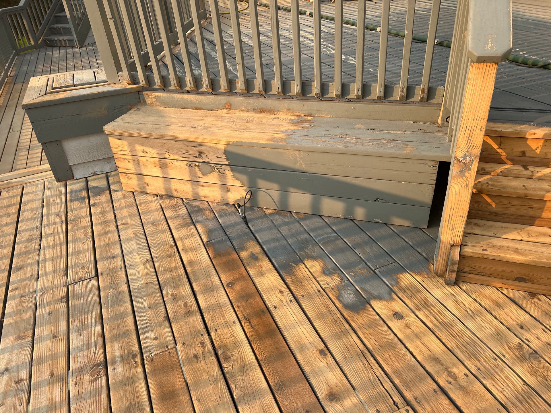 Wooden deck with steps, some painted gray, bathed in sunlight.
