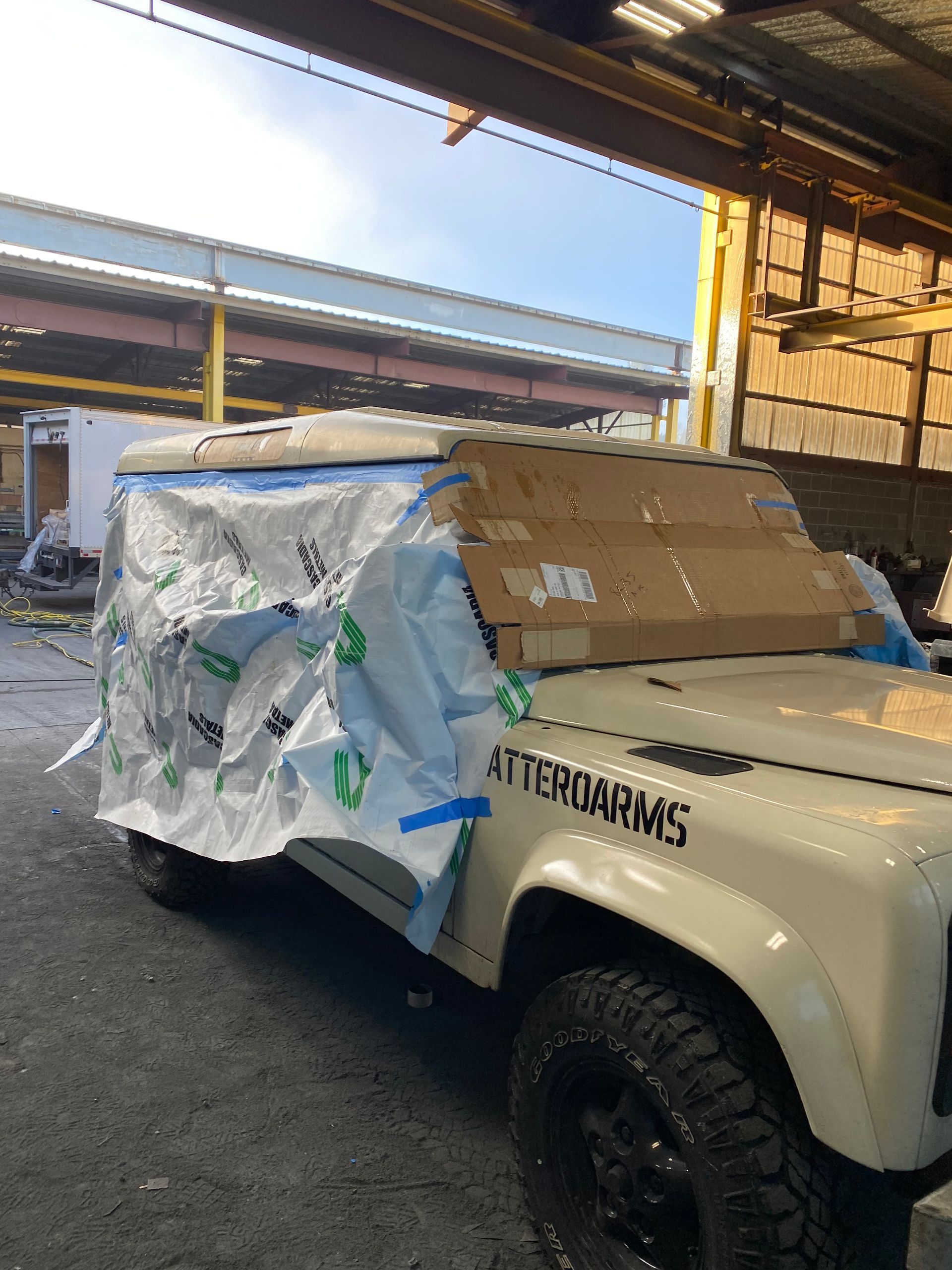 White Land Rover Defender covered in plastic and cardboard in a warehouse.