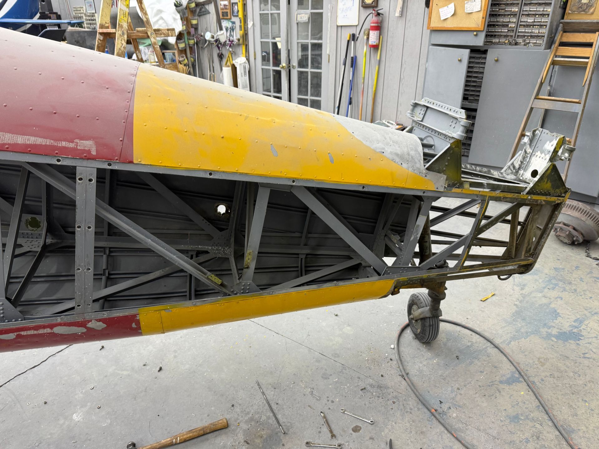 Aircraft fuselage frame with yellow, red, and silver paint, in a workshop setting.