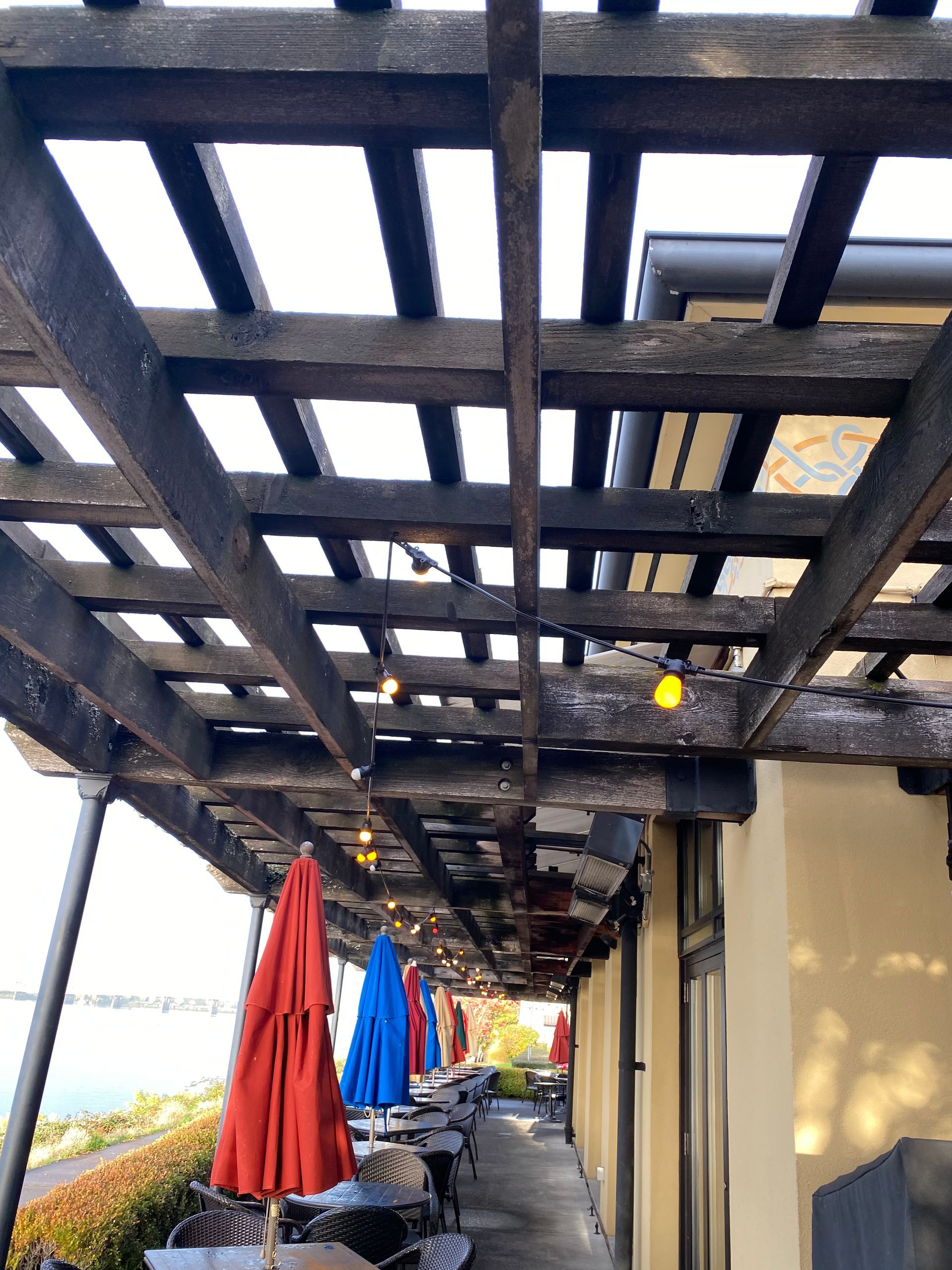 Outdoor patio with a wooden trellis, string lights, and colorful umbrellas.