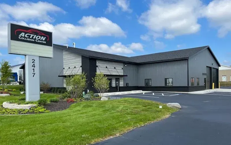 Action Car Care Center building with sign, gray exterior, asphalt driveway, and green lawn.