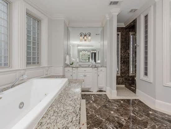 A bathroom with a tub , sink , mirror and marble floor