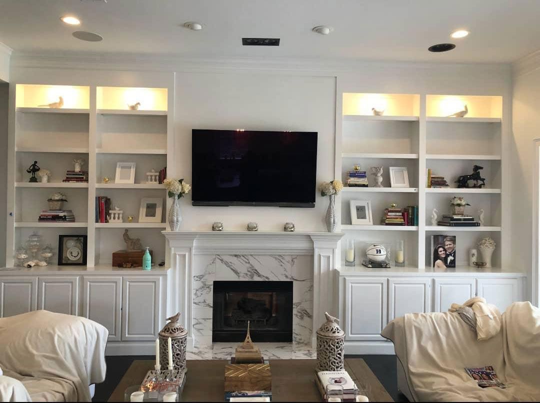 A living room with a fireplace, couch, shelves, and a flat-screen TV