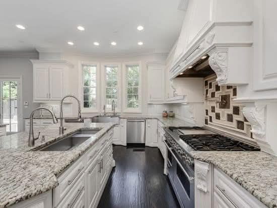 A kitchen with white cabinets , granite counter tops , stainless steel appliances and a large island