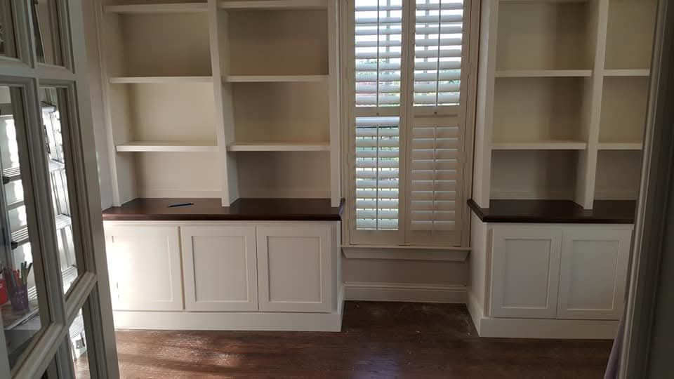 A room with white shelves and shutters on the windows