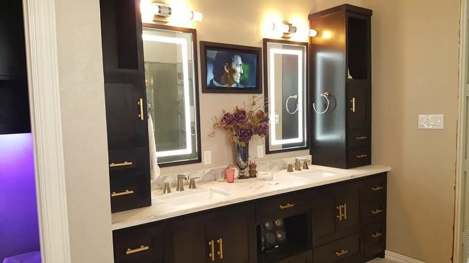 A bathroom with two sinks , two mirrors and a television