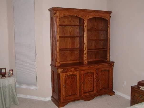 A large wooden bookcase is sitting in a room next to a window.