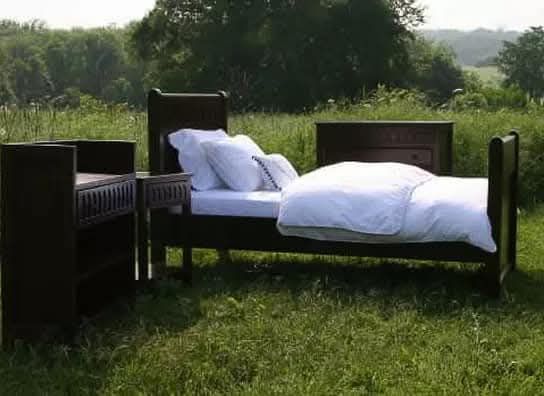 A bed is sitting in the middle of a grassy field