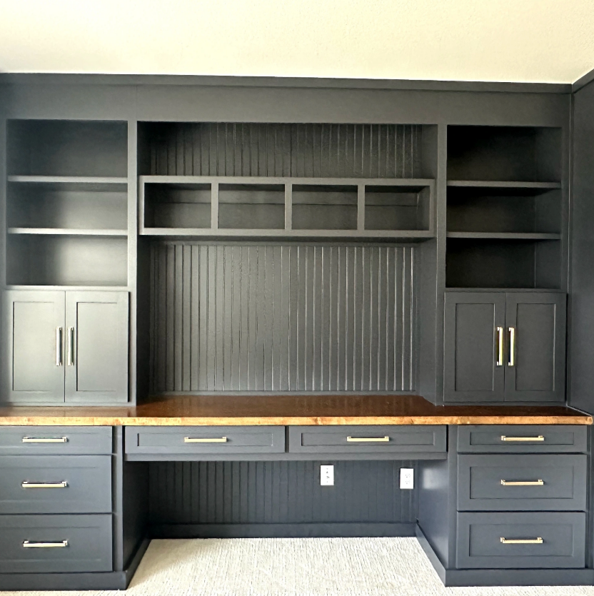 A room with a desk, cabinets, shelves, and drawers