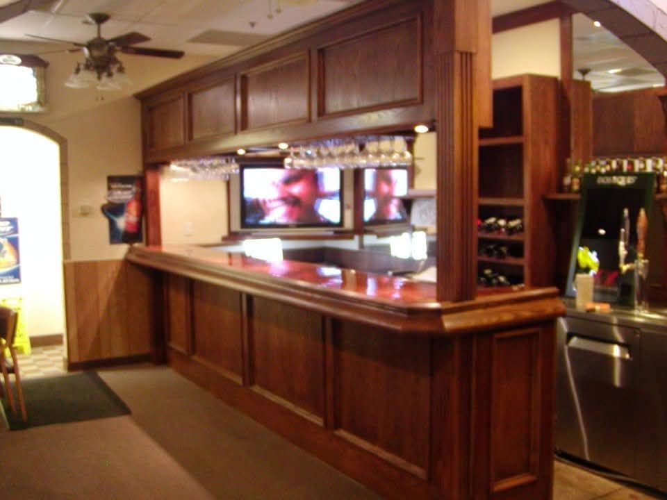 A long wooden bar in a restaurant with a tv above it