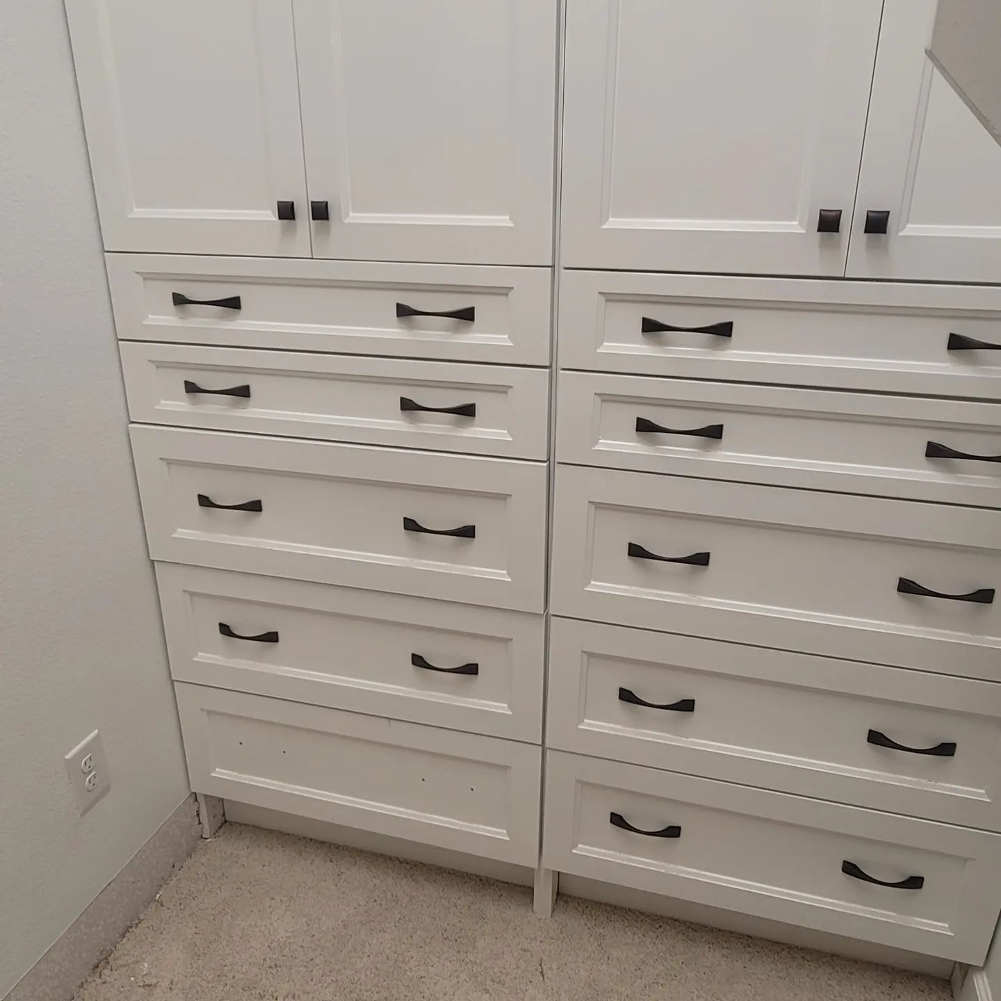 A room with white cabinets and drawers with black handles