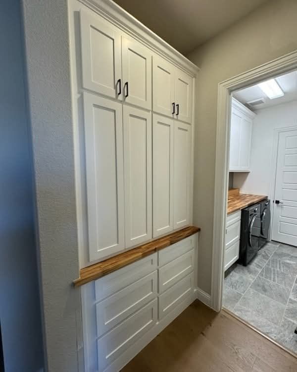A laundry room with white cabinets and a wooden counter top