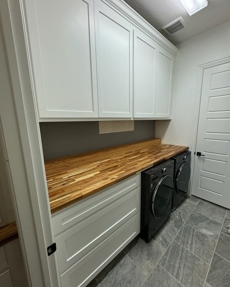 A laundry room with a washer and dryer and a wooden counter top