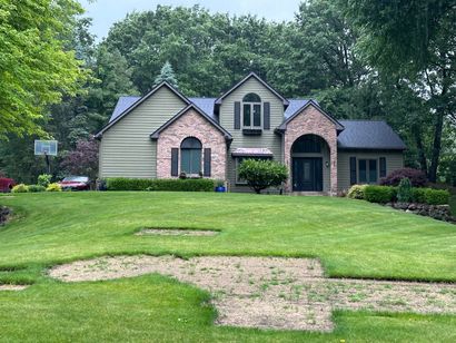 Suburban house with stone and siding facade, large green lawn, and trees in the background