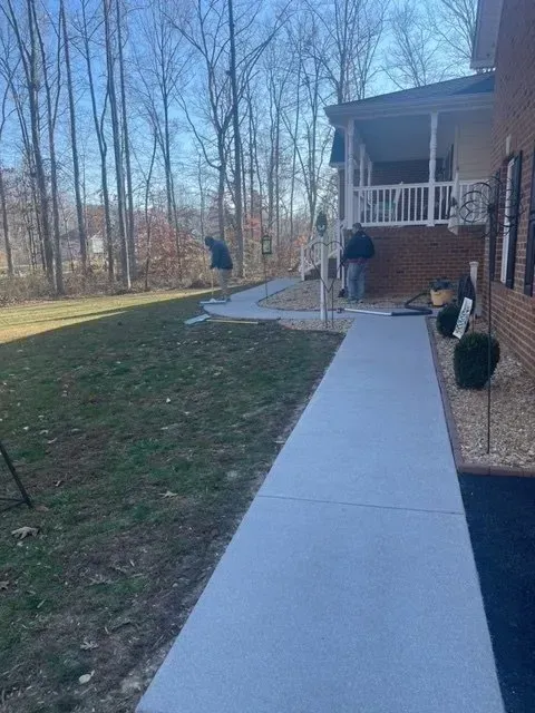 Concrete walkway leading to a porch beside a house, with two people and a yard bordered by bare trees.