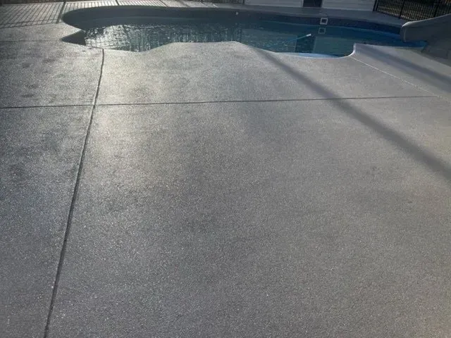 Empty concrete pool deck with shadows and curved blue-tiled pool edge