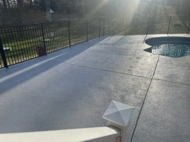 Sunlit concrete pool deck with a small pool, black fence, and a white pyramid vent in the foreground