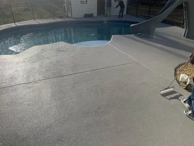 Backyard swimming pool with gray concrete deck and slide, viewed from the patio.