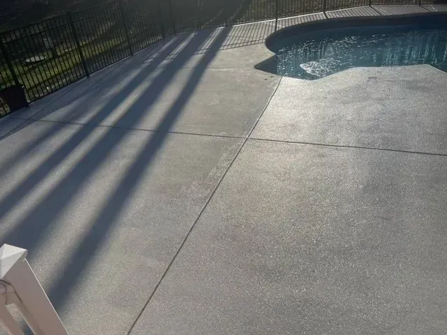 Concrete pool deck with long fence shadows beside a curved swimming pool edge