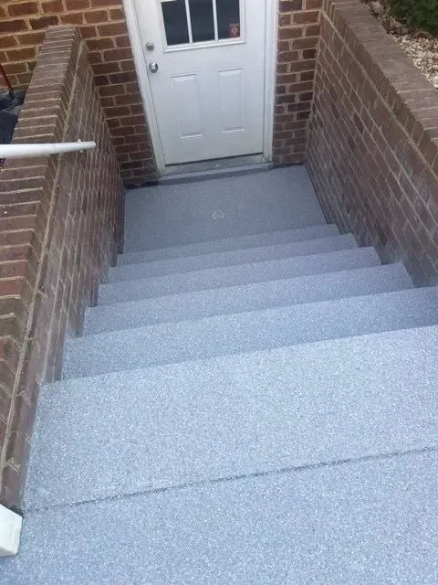 Narrow brick stairway leading down to a white door with gray steps and handrails