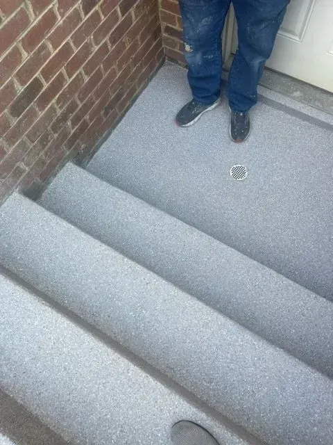 Person standing on gray carpeted stairs next to a brick wall and white door