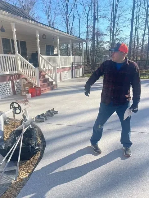 Person standing on a snowy driveway beside a house, with a red sled in the foreground.