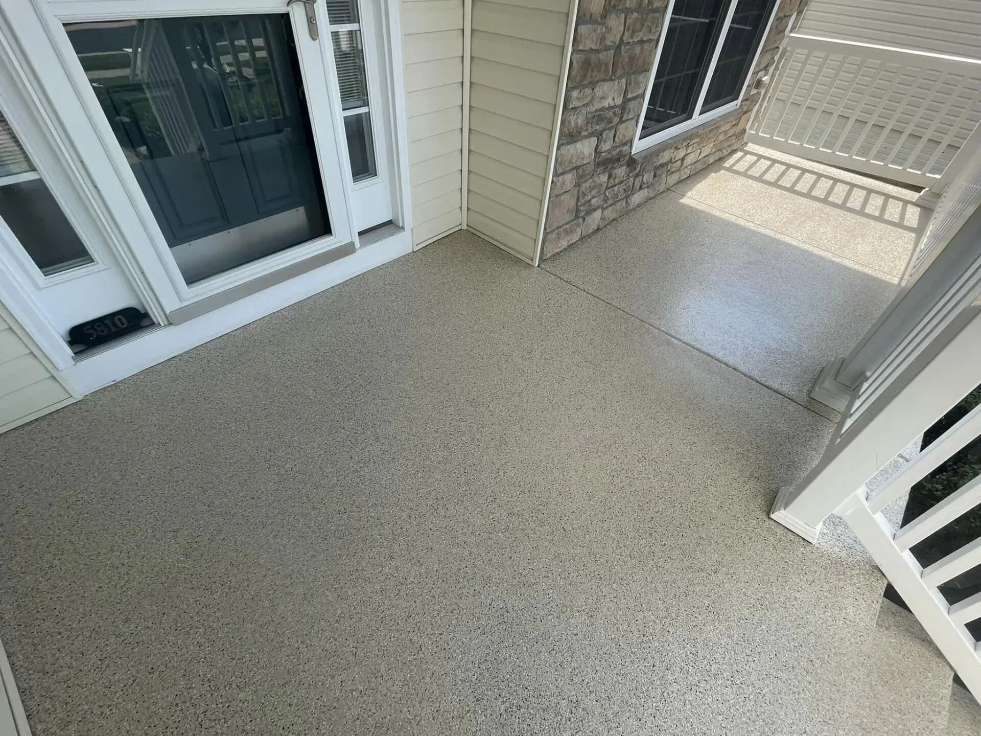 Covered front porch with speckled concrete floor, front door, and white railing.