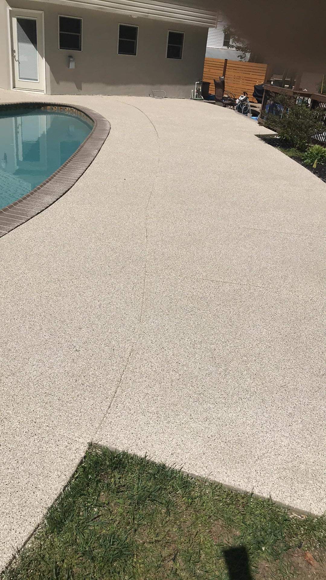 Curved poolside walkway with light pebble finish beside a swimming pool and patio