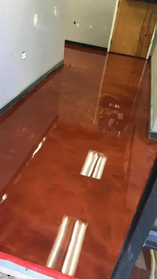 Hallway with glossy reddish-brown floor and gray walls, reflecting overhead fluorescent lights.