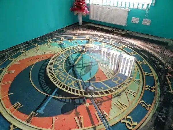 Colorful circular floor mural with clock-like design in a turquoise room near a window and radiator