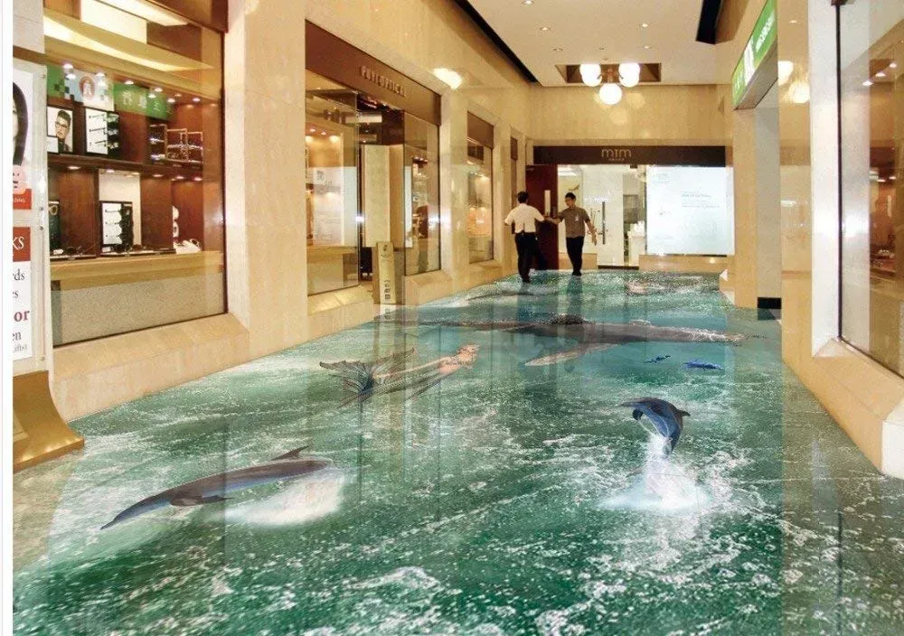 Indoor mall pool with two people standing by a turquoise water feature and swimmers visible underwater