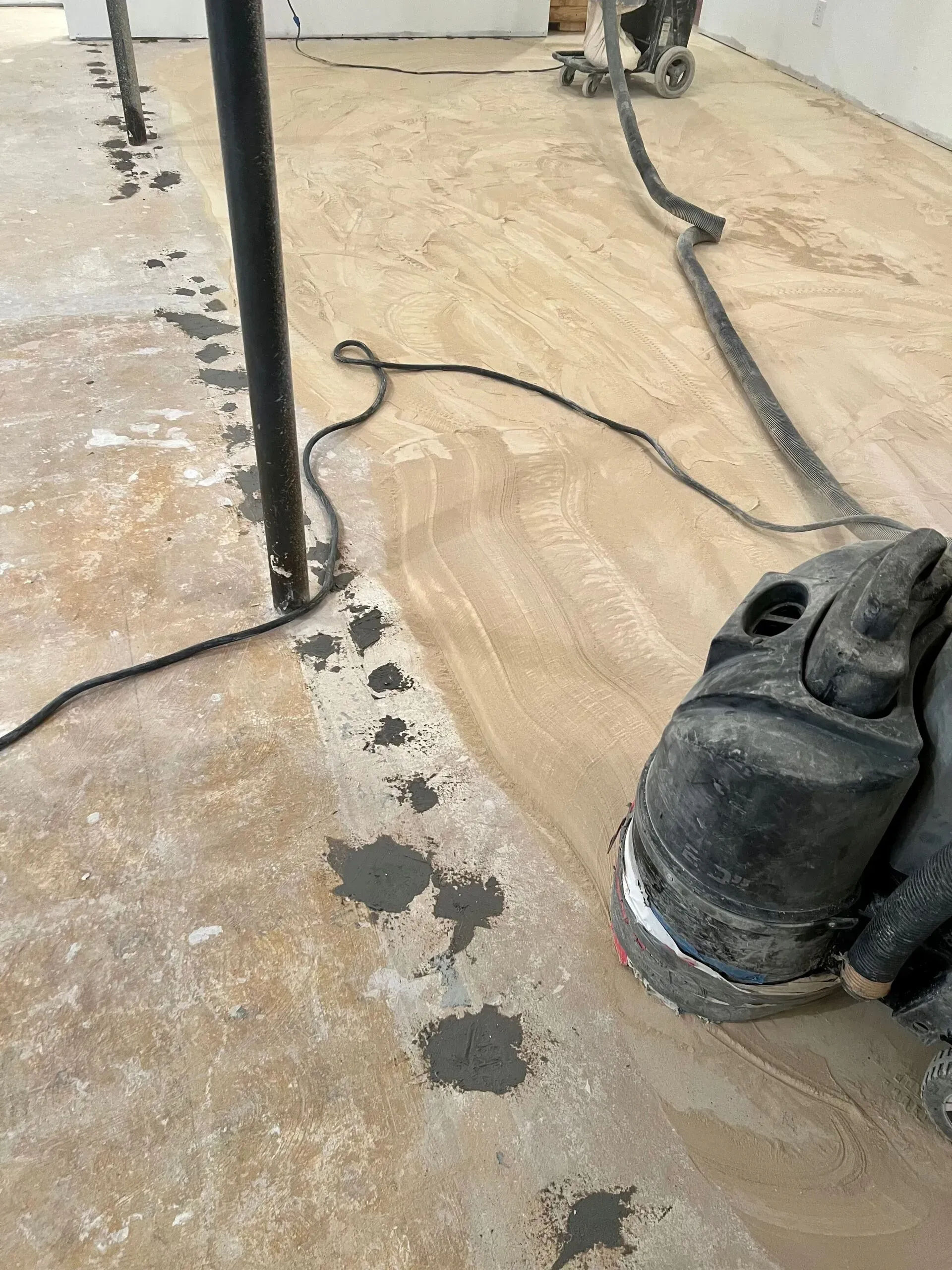 Concrete floor with a black cable, metal pole, and work boots nearby; dark patches along the edge.
