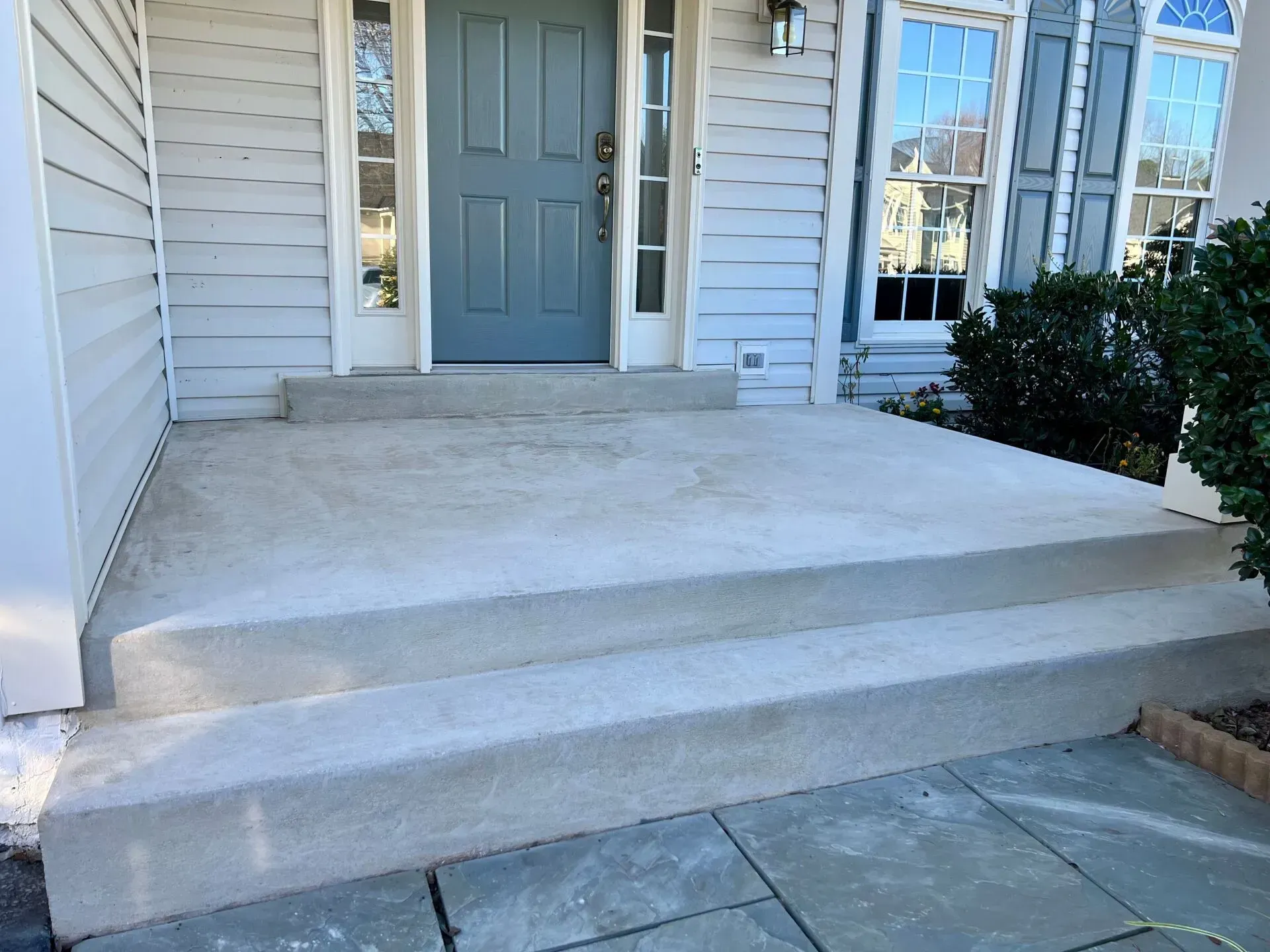 Front porch with concrete steps and ramp leading to a gray front door on a white house