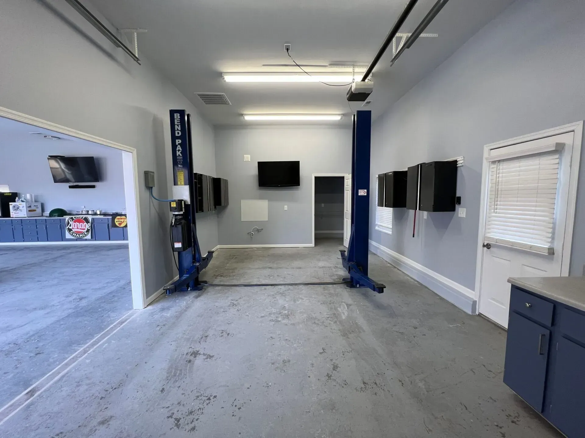 Empty auto service bay with two blue vehicle lifts, wall-mounted screens, and a front counter.