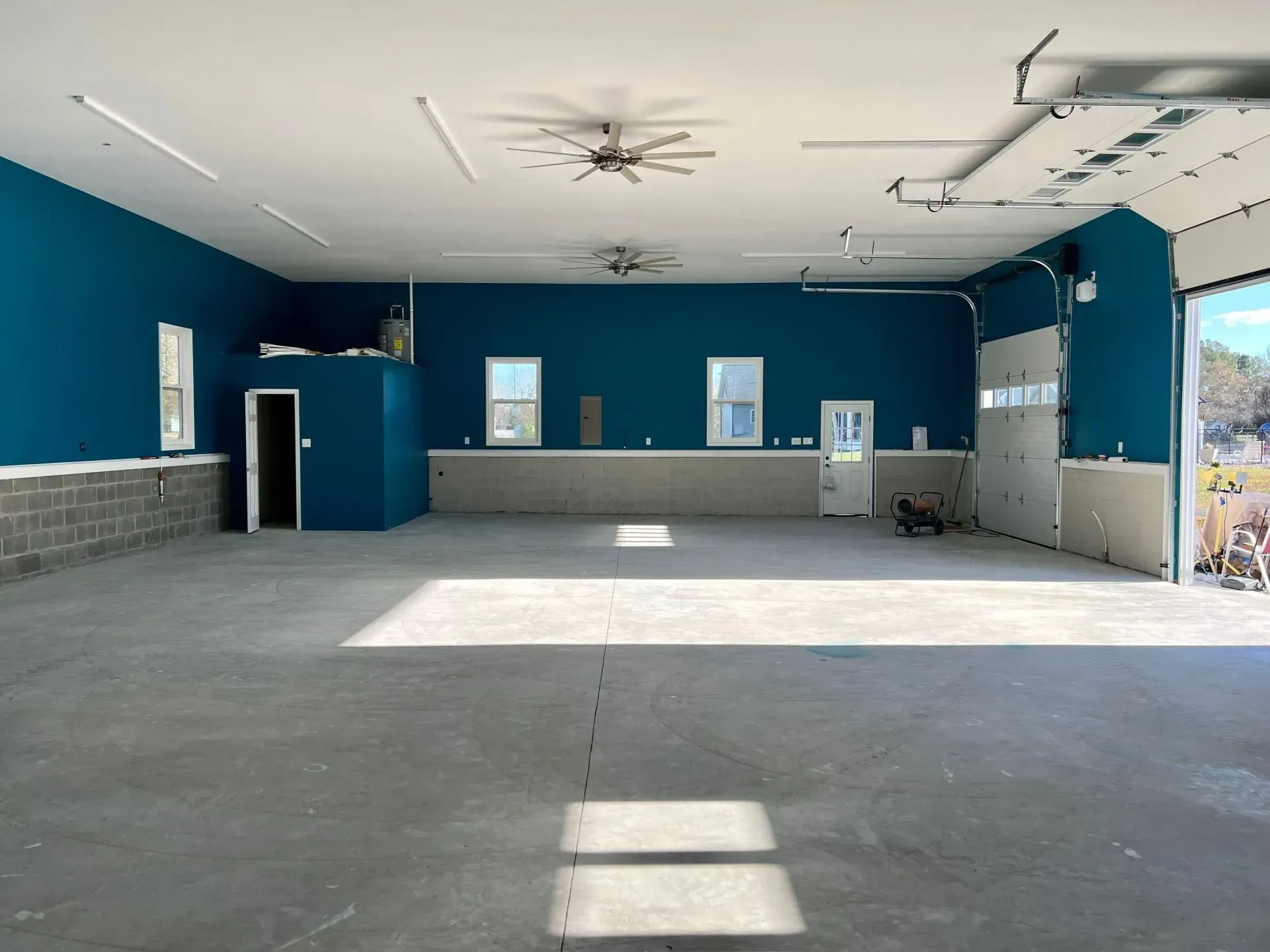 Empty blue-and-gray indoor hall with concrete floor and sunlight streaming in from open doors
