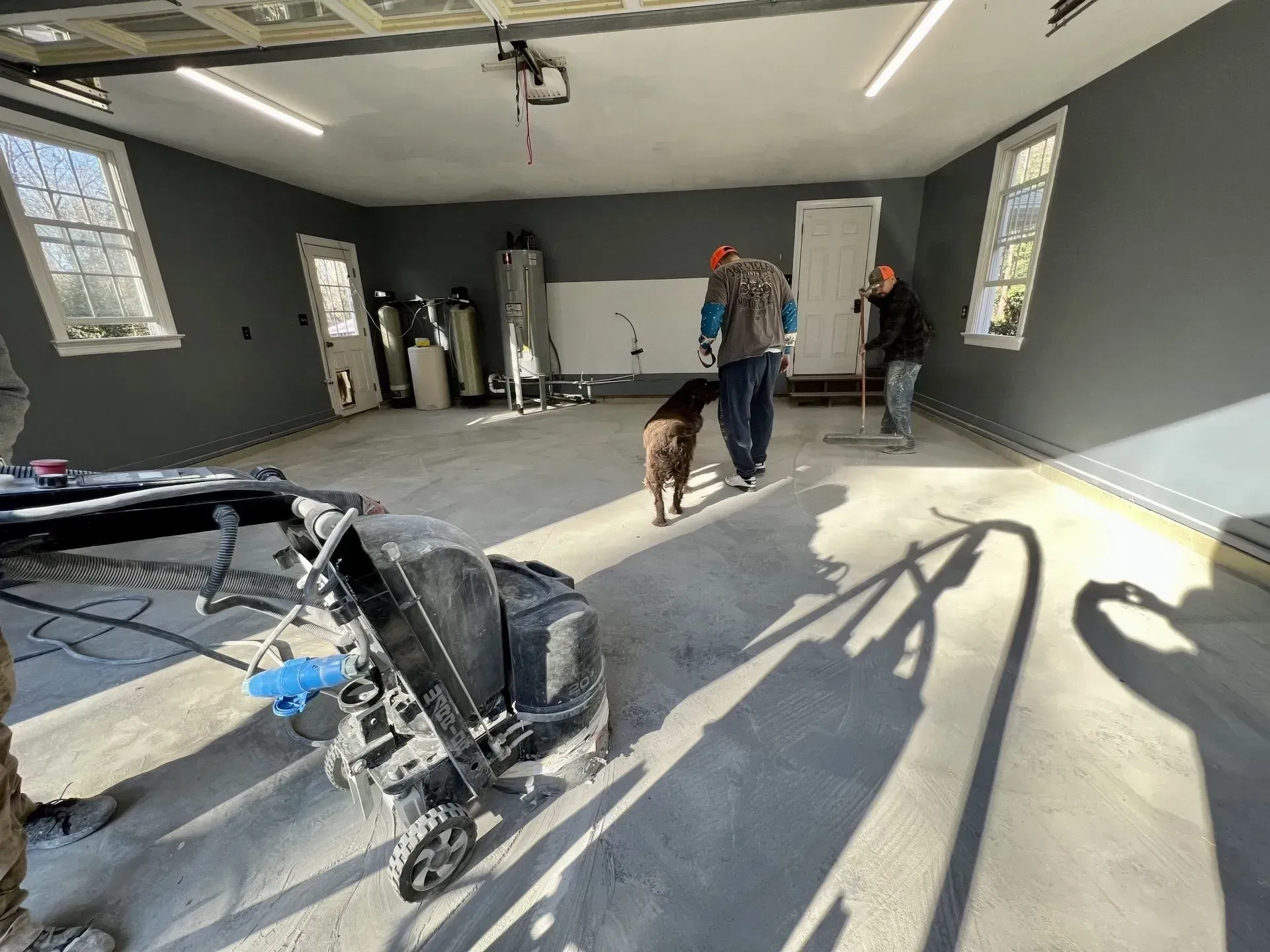 Spacious unfinished room with workers, a dog, and construction tools in bright sunlight