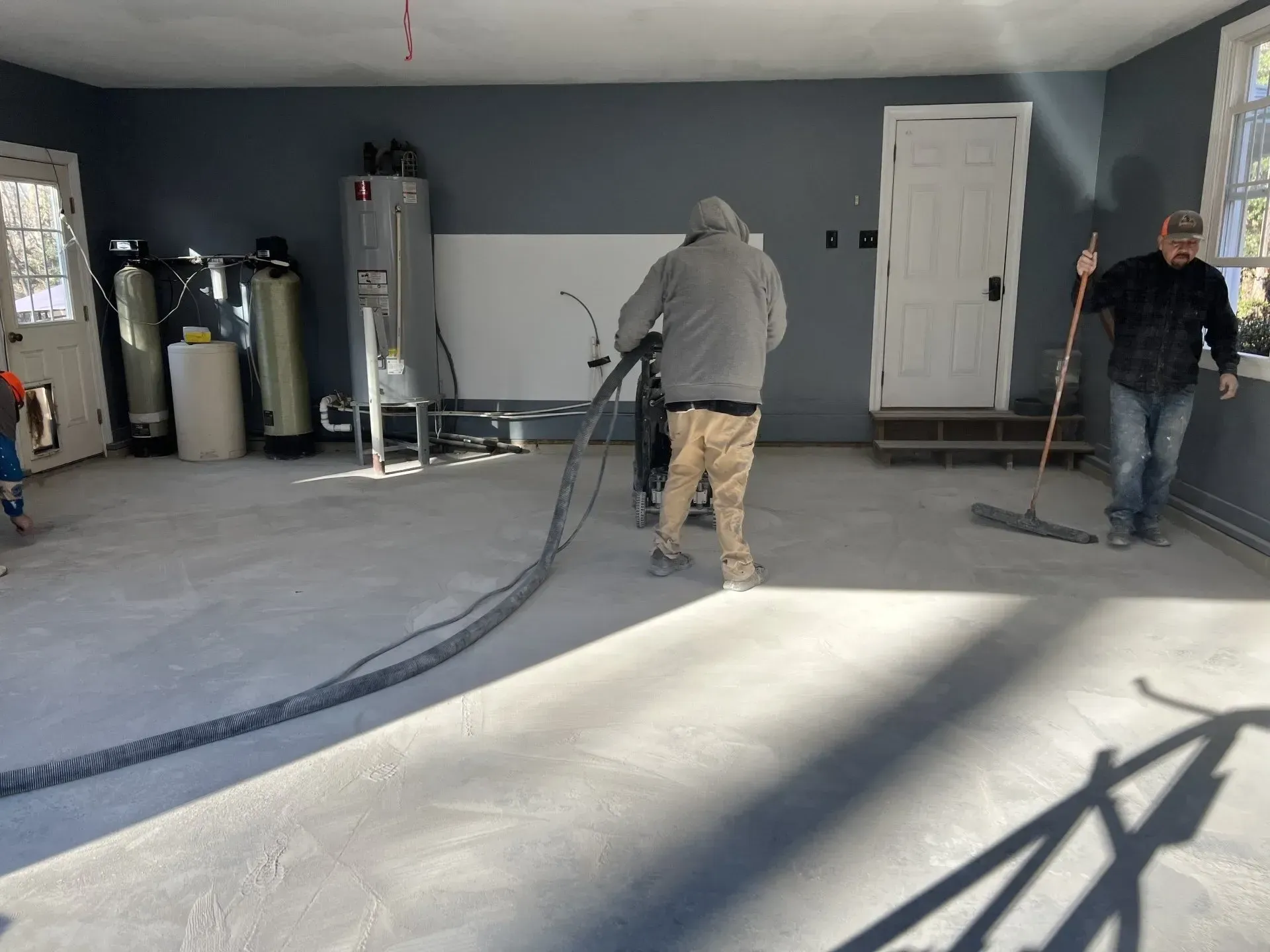 Two workers spraying insulation in a garage, with hoses and equipment on the floor.