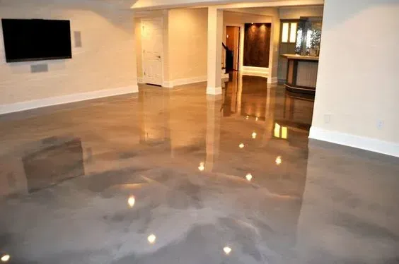 Empty modern living room with glossy gray floor, wall-mounted TV, and kitchen visible in back