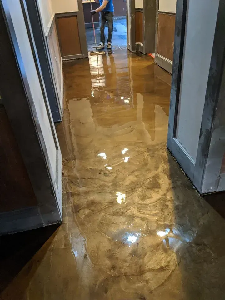Flooded hallway with standing water and a person in blue pants mopping near the end.