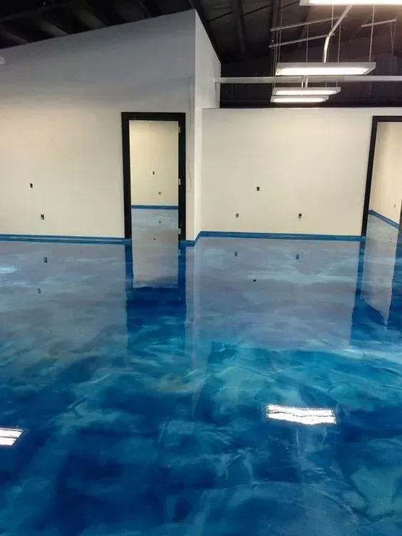 Empty room with glossy blue epoxy floor, white walls, and open doorways in an industrial space