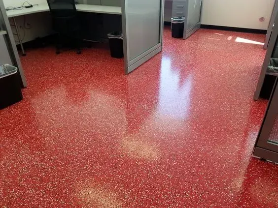 Red speckled epoxy floor in an empty office hallway with cubicles and open doors.