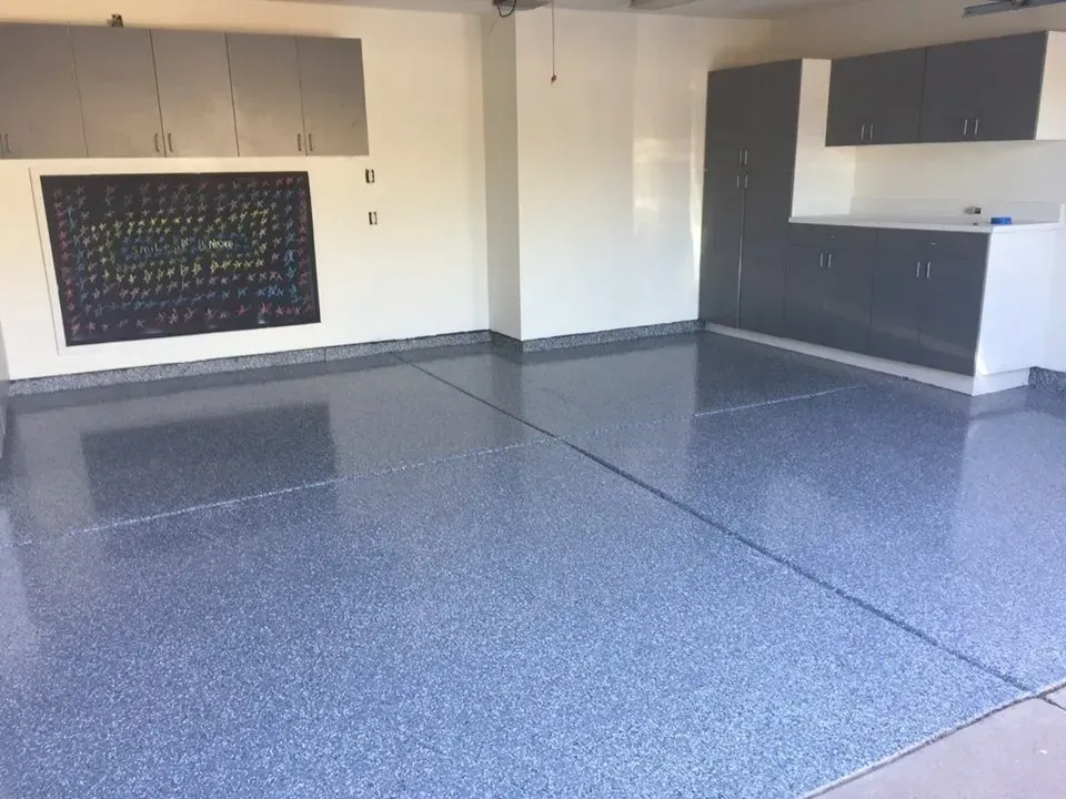 Empty modern kitchen with glossy gray flooring, white walls, and dark cabinets along the back wall.