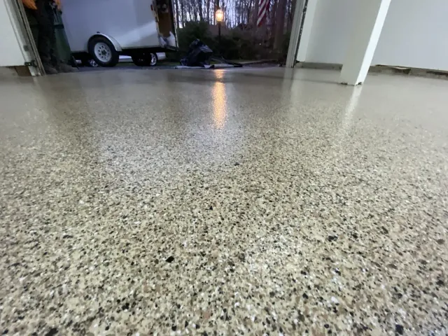 Speckled epoxy garage floor leading to an open garage with a small trailer in the background
