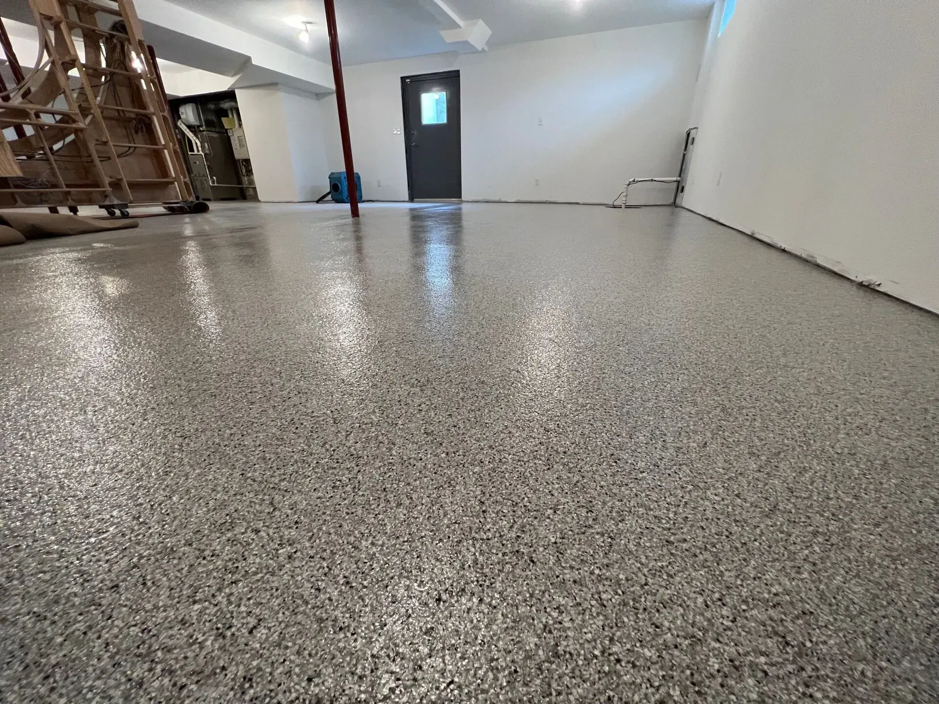 Empty garage with speckled epoxy floor, white walls, and a door in the back