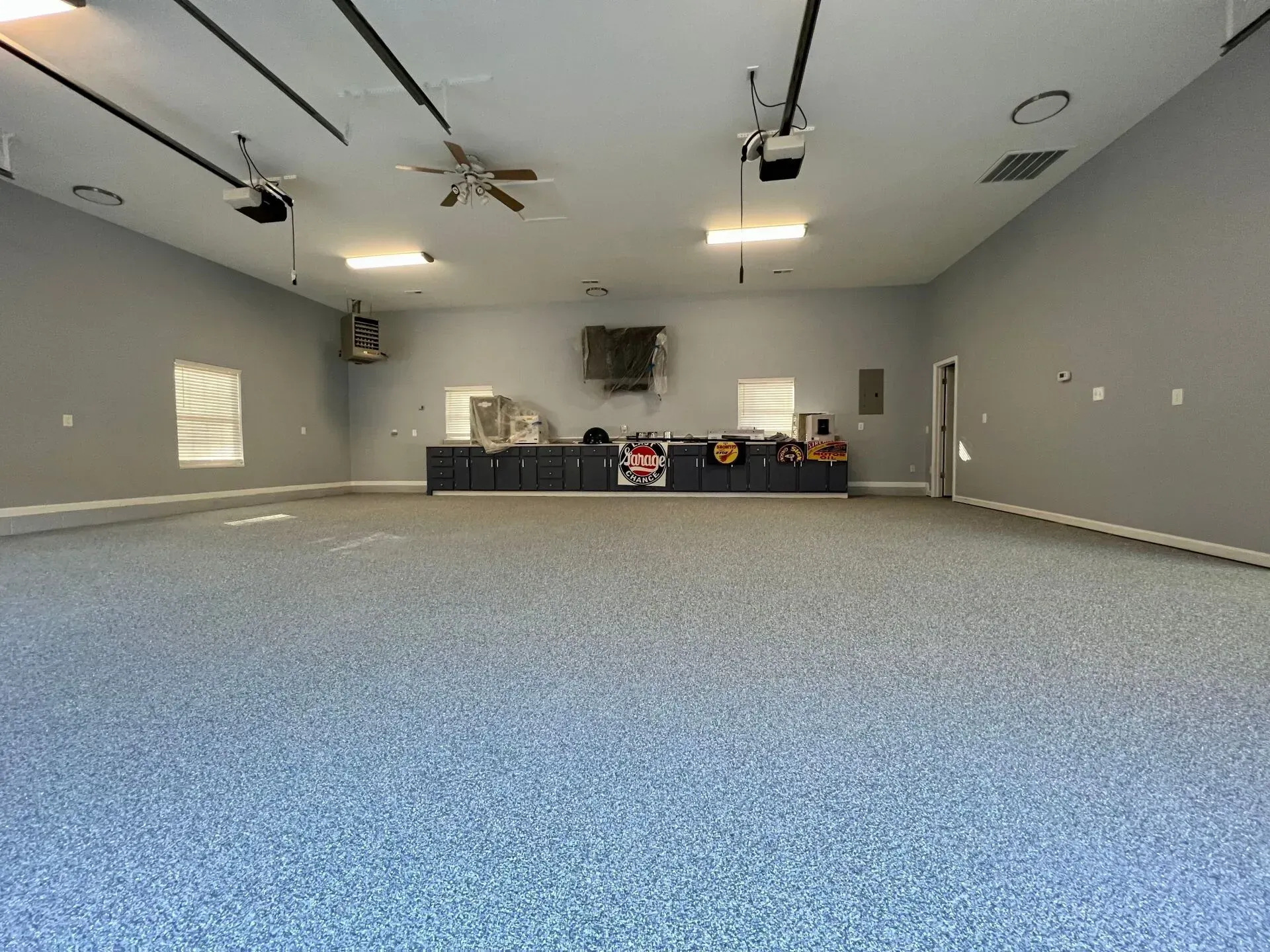 Empty gray room with blue carpet, ceiling fans, and a stage at the back