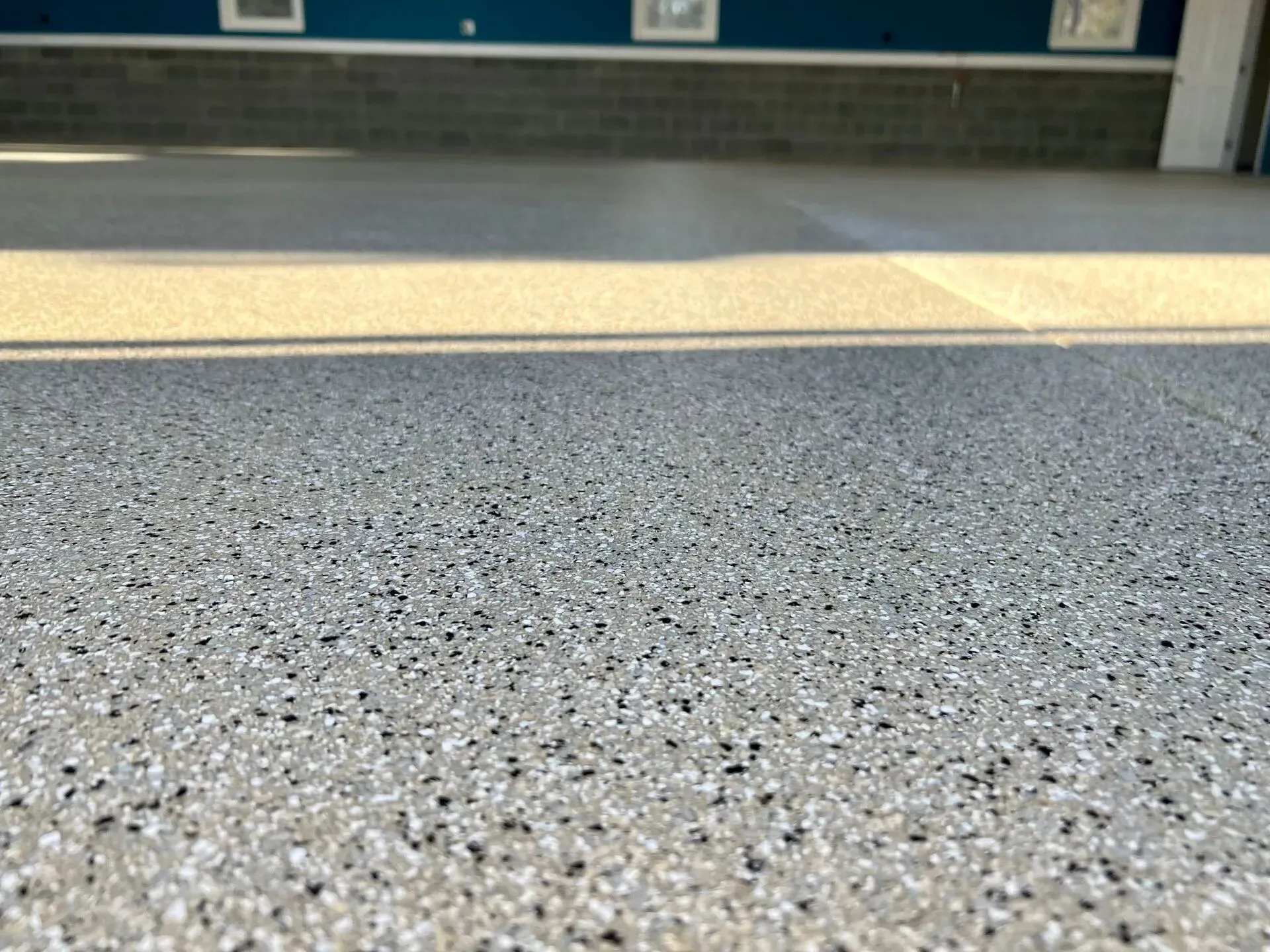 Speckled gray floor leading to a bright doorway and blue wall panels in the background