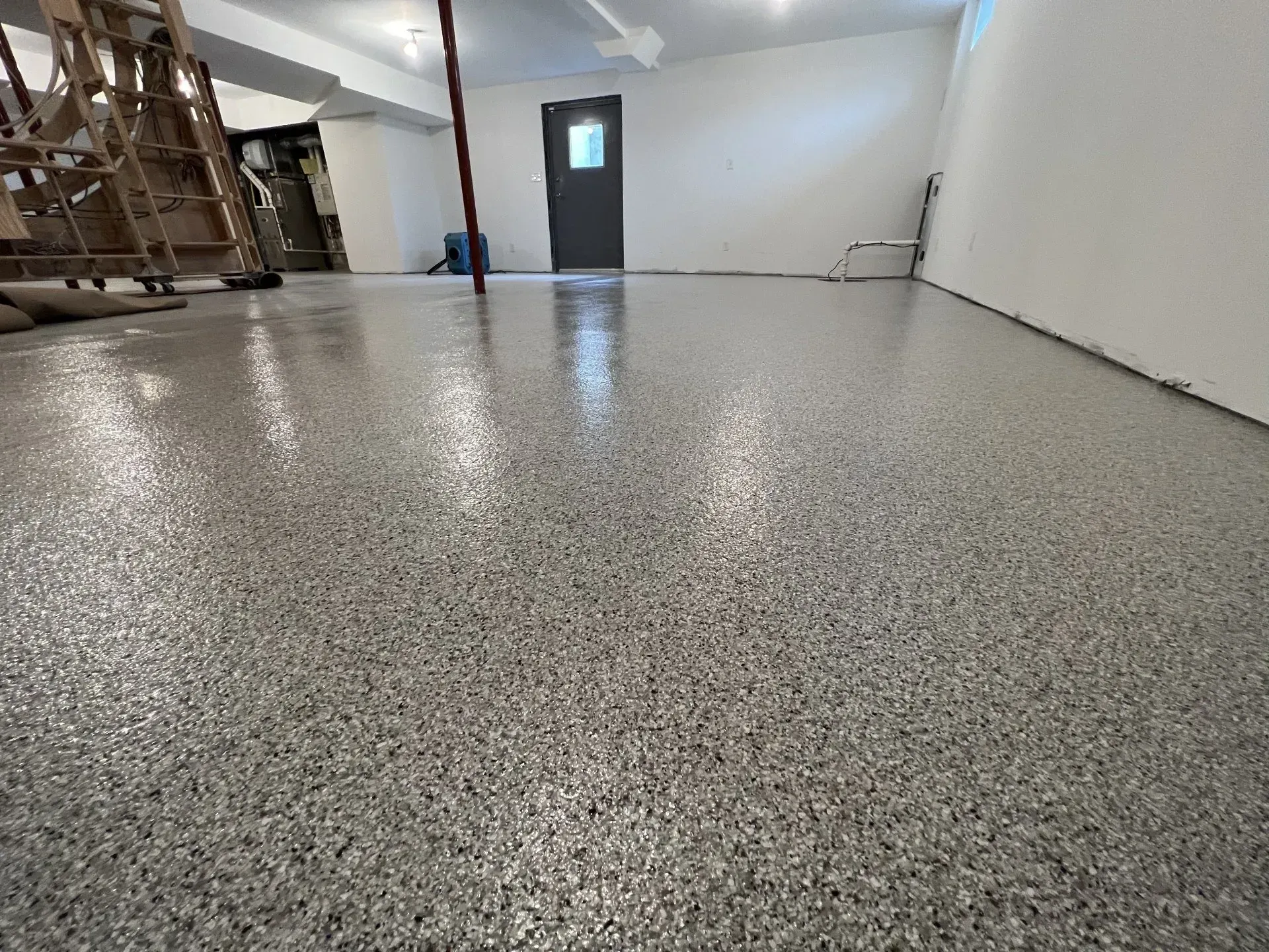 Empty room with speckled epoxy floor, white walls, and a dark door in the back.