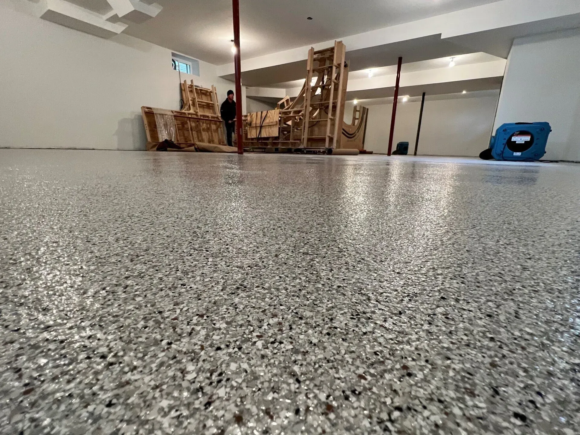 Low-angle view of a speckled floor in a room with stacked chairs and a person in the background