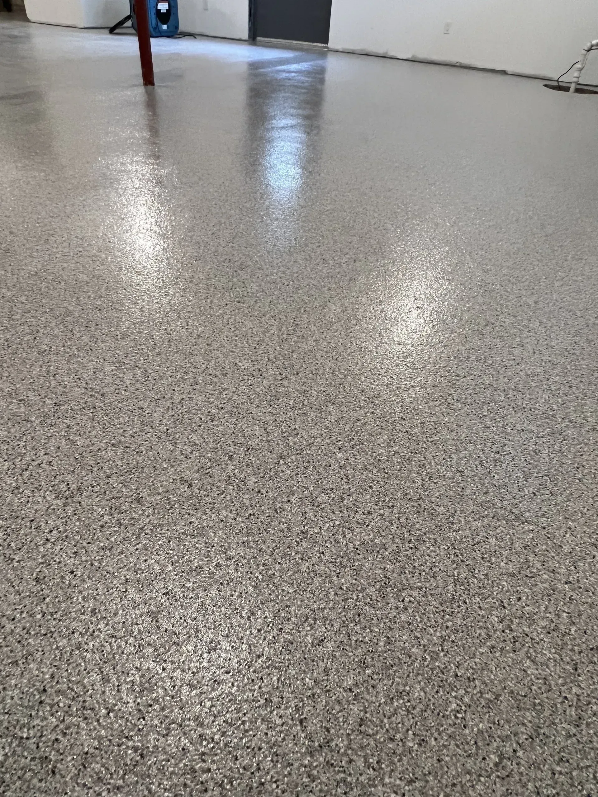 Glossy speckled epoxy floor in a room with white walls and reflections of overhead lights