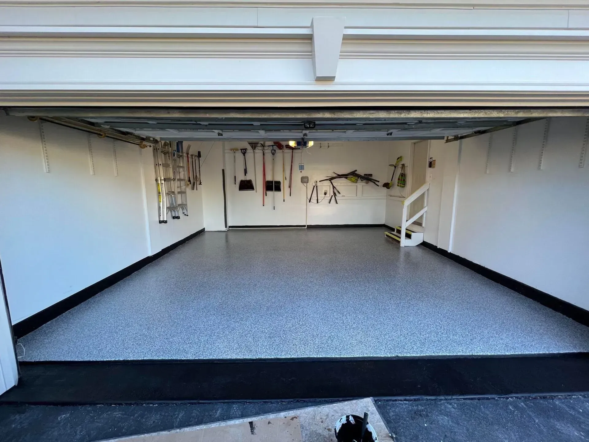 Empty garage with white walls, gray speckled floor, and a raised doorway opening to a decorated back wall